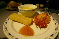  A demitasse of creamy corn and poblano soup accompanied by coconut shrimp and a vegetable spring roll with mango chutney